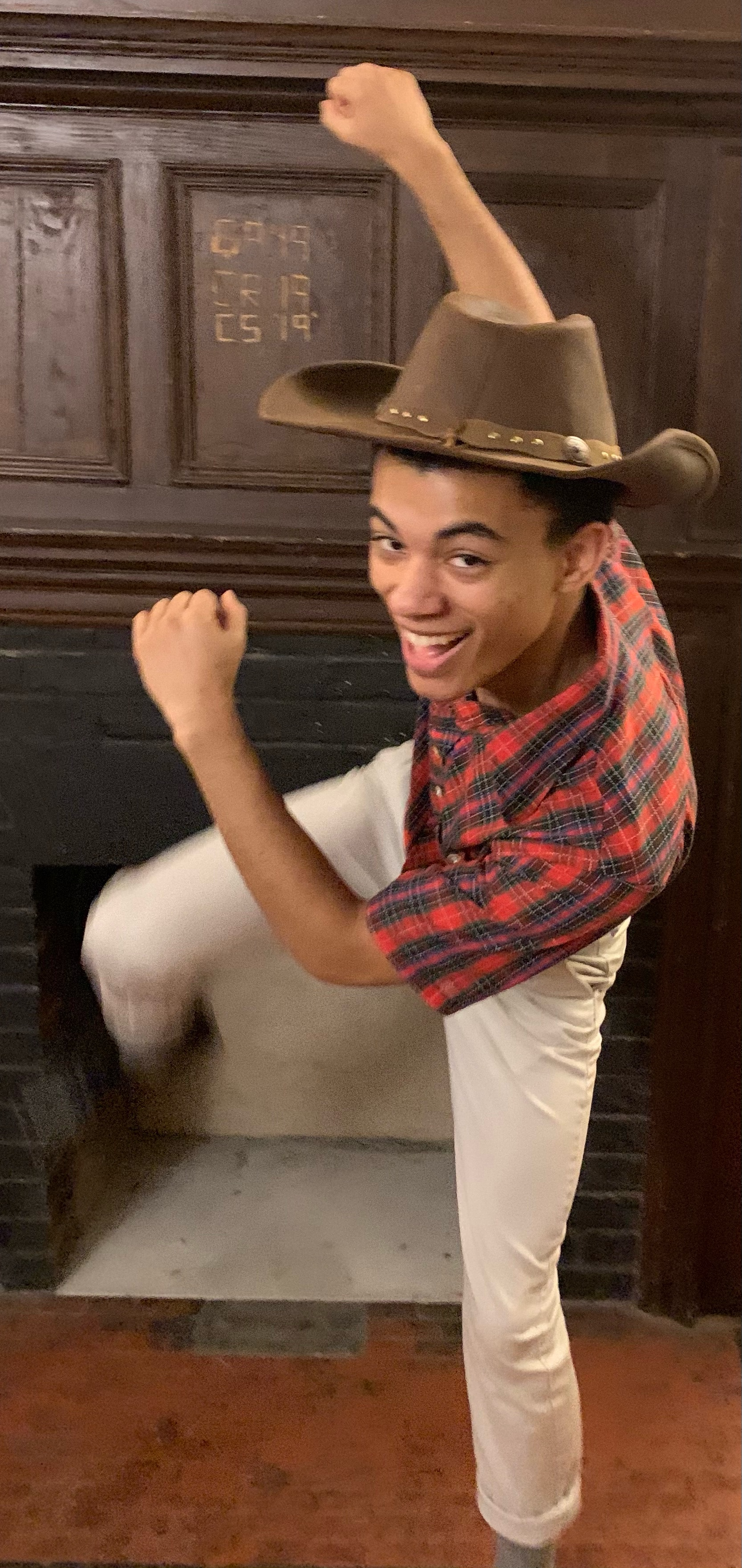 A cowboy jumping around in front of his fireplace.